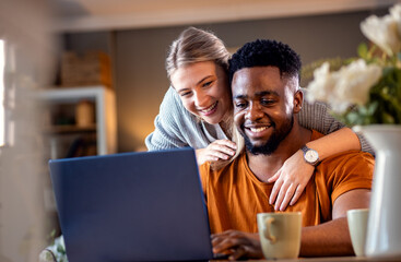 Smiling young mixed couple using a laptop while working on their home finances.
