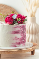 Anniversary cake with white cream cheese frosting and pink cream smears decorated with red roses on the wooden stand