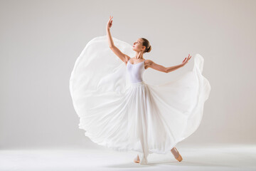 young ballerina in pointe shoes dances in a long flying white skirt on a white background