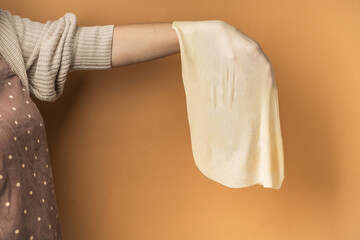 Сonfectioner in the traditional apron holding raw filo pastry on the beige warm background,...