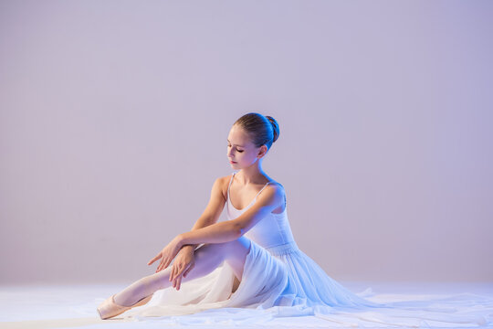 Fototapeta elegant ballerina in pointe shoes sits with her legs stretched out in a long white skirt on a white background