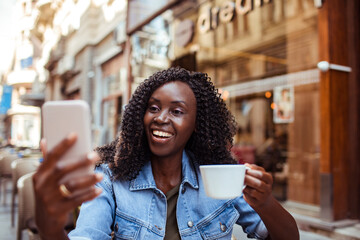Smiling young woman sitting in street cafe using smartphone