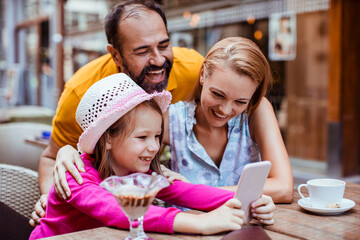 Little girl holding cell phone with parents in outdoor cafe