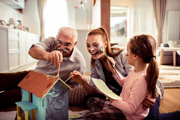 Grandfather, Mother, and Daughter Painting Small House Together at Home