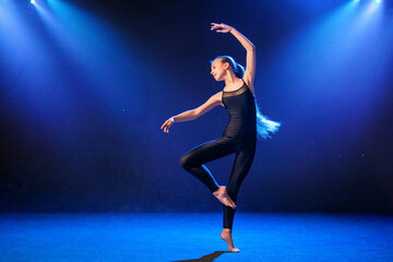 teenage girl in a tight black costume dances as a modern dancer isolated on the background in neon light.