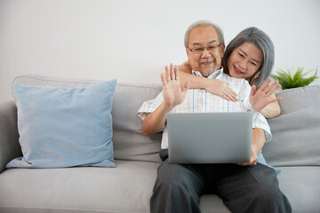 senior couple using laptop computer and online video call say hello or goodbye with family on sofa