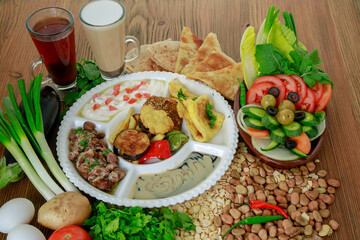 Egyptian Dynamite breakfast platter with flafel, marinated fried eggplant, omelette, hummus, foul, beans, pita bread, salad and coffee drink isolated on table side view