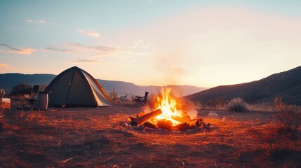 Camp fire, tent and mountains in the background at sunset