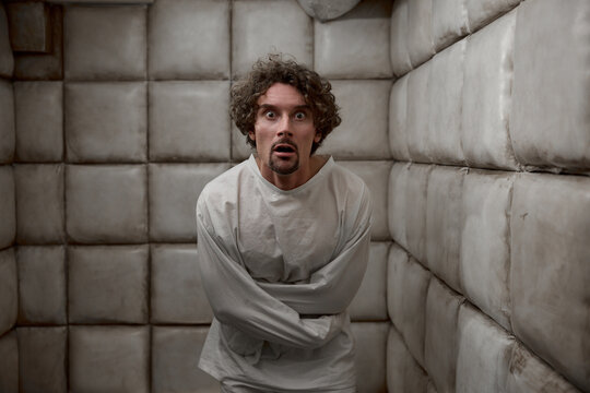 Scared man with schizophrenia mental disorder in white padded room