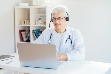 Middle aged male doctor using headset and laptop for online video call consulting of patient. Telemedicine concept for domestic health treatment. Online remote medical appointment. Medical technology