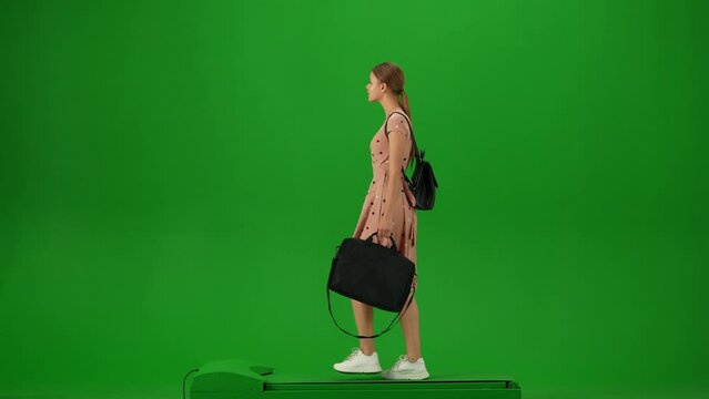 Portrait of traveler isolated on chroma key green screen background. Young girl in dress walking with laptop bag and looking around.