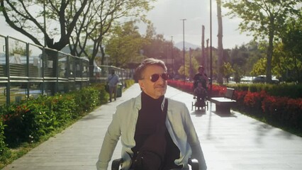Disabled happy middle aged man user wheelchair. Arab handsome man walking in park area in sunny day. - Powered by Adobe