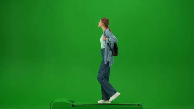 Portrait of traveler isolated on chroma key green screen background. Young girl in jeans with small backpack walking and looking around.