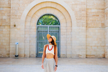 Fototapeta na wymiar A young girl in a hat and with a backpack walks among old buildings. travel and adventures in Israel. Haifa.