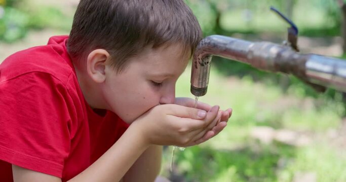 Child boy drinking water from water the tap outdoors