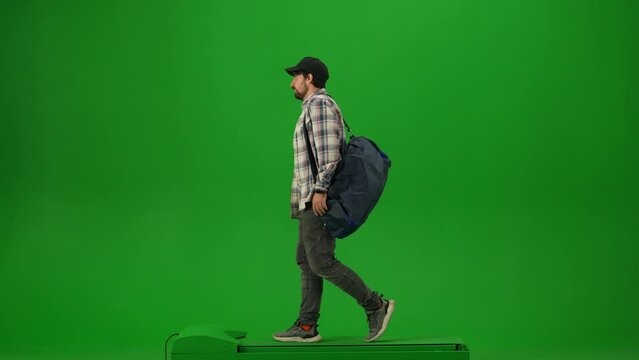 Portrait of traveler isolated on chroma key green screen background. Adult man with sport bag in cap walking and talking on smartphone.