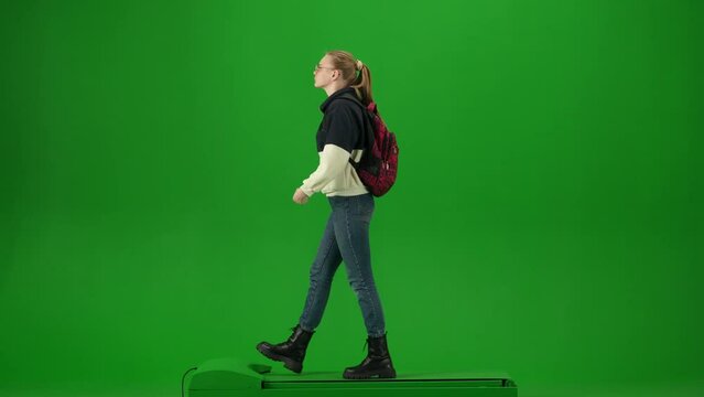 Portrait of traveler isolated on chroma key green screen background. Young girl in glasses with backpack walking and looking around.