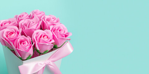 Artificial lilac rose flowers in a white box with a bow on a blue background. Close-up. Horizontal photo