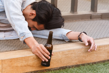 Alcoholic asian man drink beer from the bottle sitting on the floor after party. Sad heartbroken...