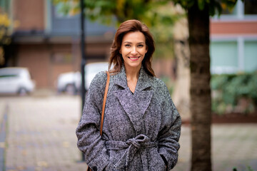 Fototapeta premium Brunette haired woman wearing tweed coat and walking outdoors in the city street on autumn day