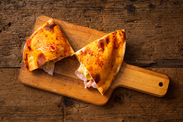 open baked calzone with cooked ham and artichokes on wooden cutting board