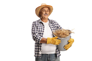 Happy mature farmer holding a bucket full of hay