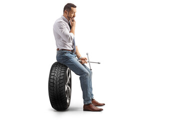 Profile shot of a pensive man sitting on a car tire and holding a lug wrench