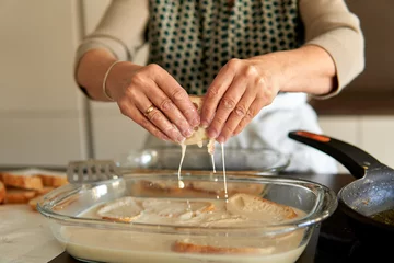 Foto op Canvas Close up of senior woman hands holding bread with sweet milk and cinnamon to make traditional torrijas recipe. Making traditional recipe on a contemporary electric stove © Komuso & Colorsandia