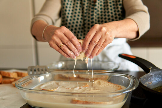 Close up of senior woman hands holding bread with sweet milk and cinnamon to make traditional torrijas recipe. Making traditional recipe on a contemporary electric stove