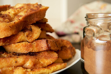 stack of home made torrijas or torrejas, typical latin french toasts for Lent and Easter near a glass jar with cinnamon powder
