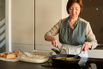 Happy grandmother frying spanish torrijas french toasts on oilve oil for easter