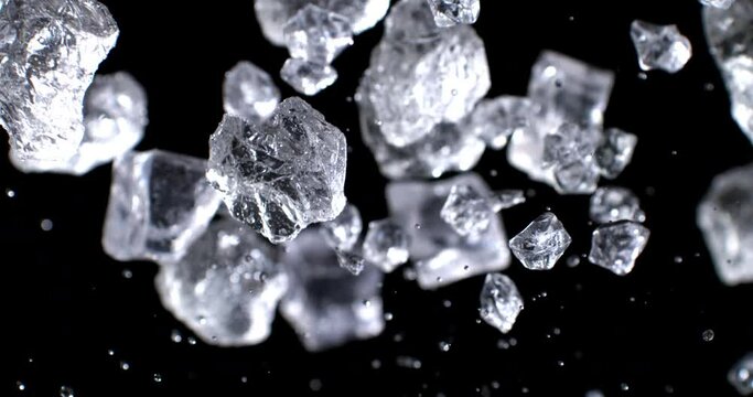 Super slow motion top view close up of ice cool cubes are flying with splashing water drops in transparent clear glass with pure fresh crystal liquid isolated on black background