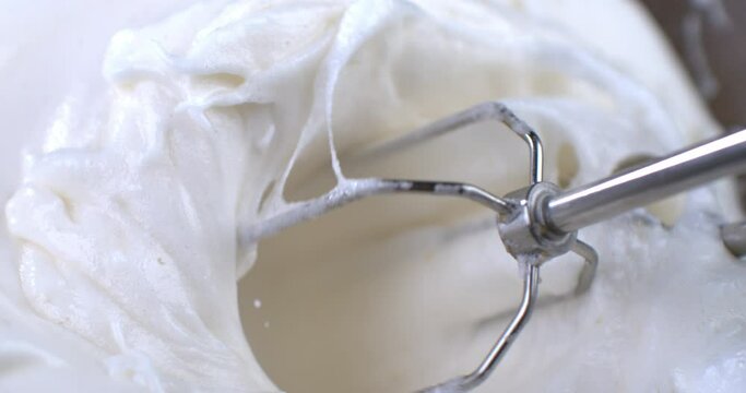 Super slow motion macro of electric mixer whisks a whipped cream from fresh bio organic milk for sweet holidays dessert preparation at 1000 fps.