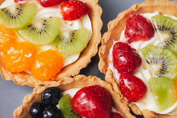 Fruit tartlet background. Strawberries, kiwi, blueberry and mandarin. Small tartlets on a plate. Dessert background. Mini cakes for banquet. Homemade pastry. Summer little pie.