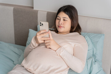 Pregnant asian woman holding smartphone at home using mobile app for pregnant women