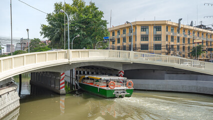 Location photos A bridge crossing the river and canal in the heart of the city with buildings and green trees along the banks. There is a passenger ship passing through the channel under the bridge. 