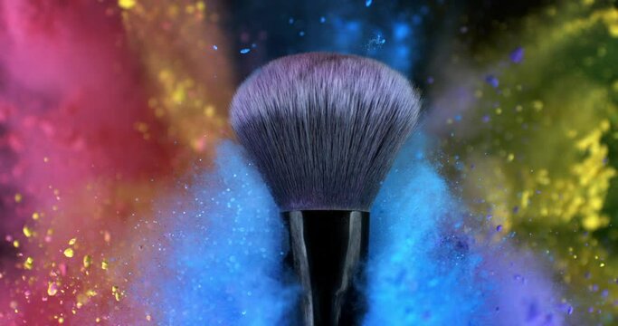 Super slow motion macro of makeup brush with flying rainbow colorful cosmetic product powder dust glitter particles splash explosion isolated on dark background.