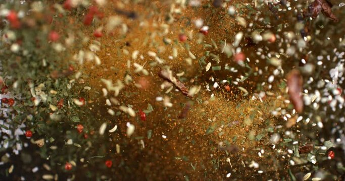 Super slow motion macro of falling heap of granulated rough crystal salt, peppercorn and other mixed herbal spices with flying grains at 1000 fps.