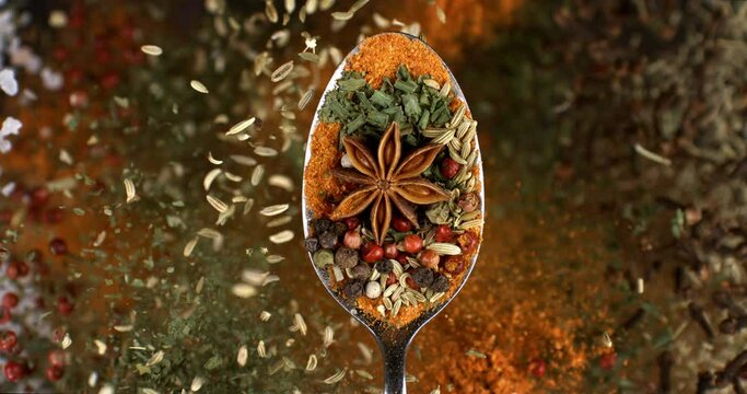 Super slow motion macro of dry pink flavorful aromatic peppercorn seeed and other spices mix falling down from silver spoon isolated on soft dark background.
