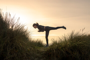 Side view of woman performing warrior III yoga pose at sunrise.