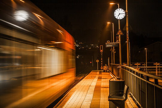 Nächtlicher verlassener Bahnsteig mit Bahnhofsuhr und abfahrendem Zug im Schummerlicht
