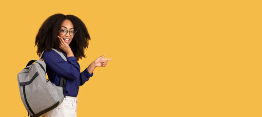 Surprised black student girl pointing to the side on yellow background