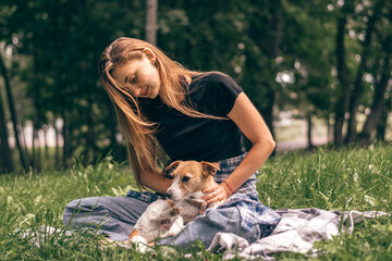 A young positive woman hugging friendly Jack Russell Terrier dog, enjoying happy moments together while walking in the park on a summer day.
