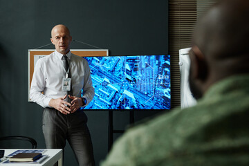 Focus on mature male coach or officer in formalwear standing by interactive screen in front of...