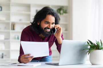 Indian man multitasking with phone and laptop while working at home office