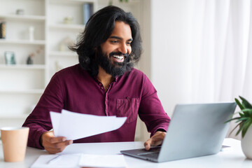Handsome Indian freelancer guy working on his laptop and checking documents