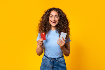 Happy shopper with credit card and phone on yellow