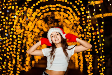 A young, beautiful girl walks in a Santa hat, in the evening city, decorated with New Year's lights