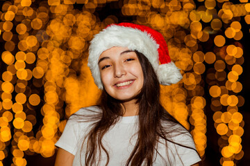 A young, beautiful girl walks in a Santa hat, in the evening city, decorated with New Year's lights