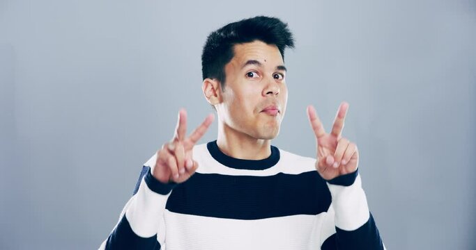 Face, emoji and peace sign with an asian man in studio isolated on gray background for freedom. Smile portrait, social media or v hand gesture and a happy young person posing for a profile picture